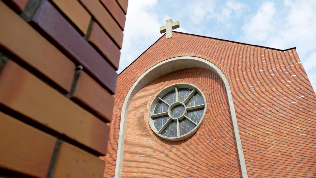 Facciata di chiesa che appare da dietro un muro di mattoni alla luce calda del giorno.