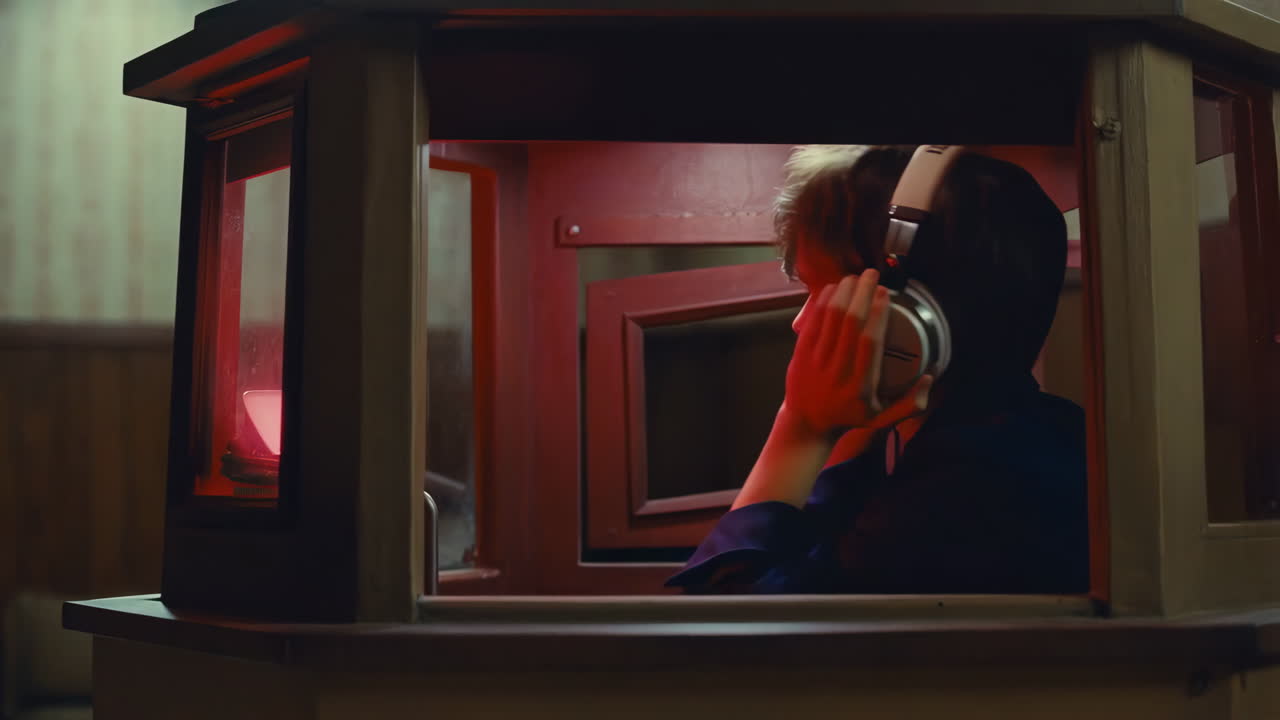 Person Listening with Headphones in a Red-Lit Booth
