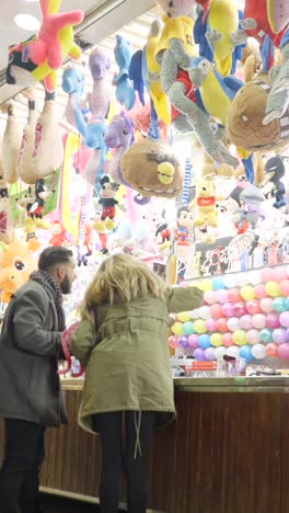 People playing carnival games surrounded by stuffed animal prizes