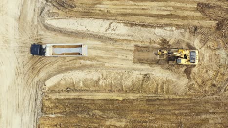vista aérea de arriba hacia abajo de una excavadora que carga piedra triturada en un camión volquete en una cantera de piedra triturada