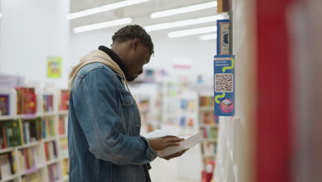 young man holding open book, examining pages, focused, standing in modern library with bookshelves filled with colorful books, bright indoor lighting, casual attire