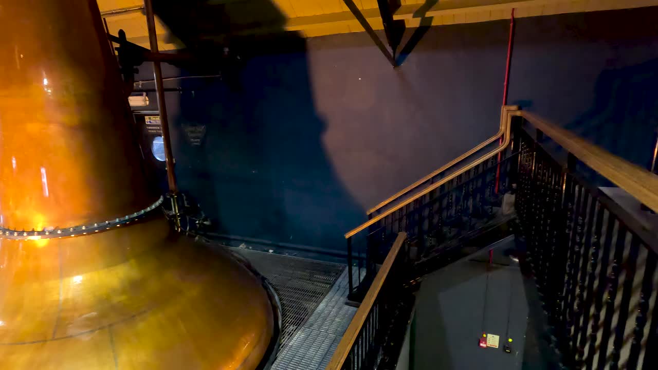 Camera pans copper pot stills in warmly lit distillery, highlighting industrial craftsmanship and traditional process