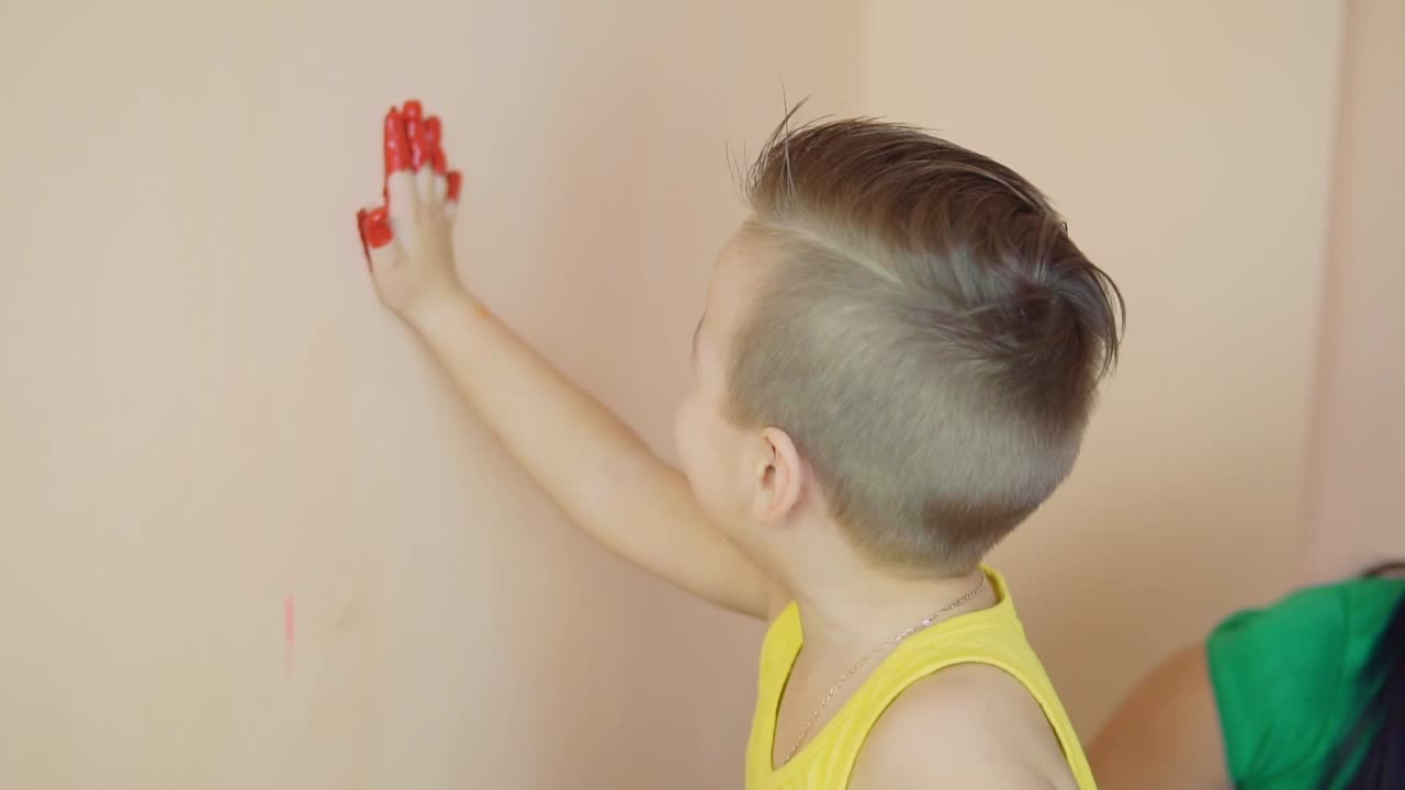 счастливый милый мальчик веселится, оставляя красные отпечатки рук на стене. молодая счастливая семья. концепция матери и ребенка