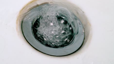 soapy water flowing down the drain of a sink in the bathroom - high angle, close up
