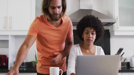 Mixed-race-couple-using-laptop-and-calculating-finances-in-the-kitchen-at-home
