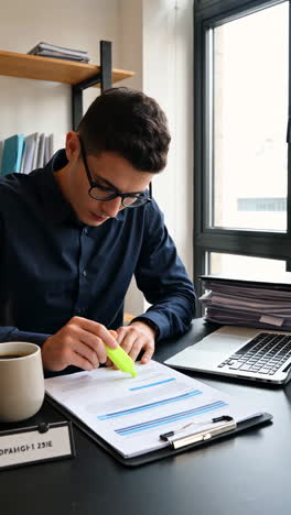 young man highlighting document at desk