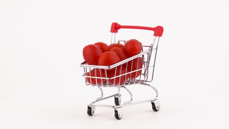 el carrito de compras lleno de tomates de uva roja se acumula con gotas de agua. girando en la mesa giratoria. aislado en el fondo blanco. primer plano. macro.