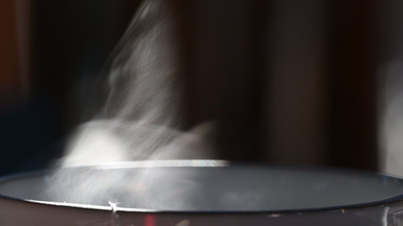 뜨거운 차 한 잔에서 증기가 빠져나가고, 흰색 입자가 증발하고, 태양에 비추어집니다.