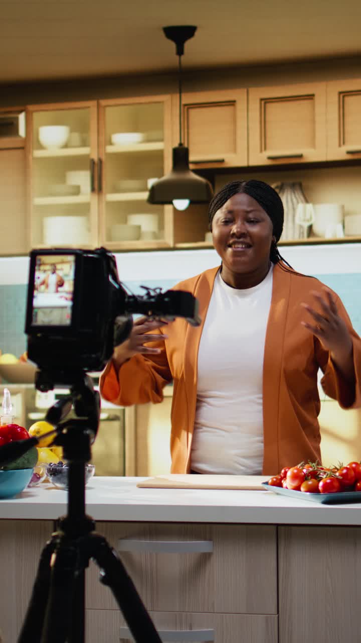 Vertikal video: Bag kulisserne af kvinde der optager en meal prep vlog med stativ i køkkenet.