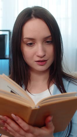young excited woman reading book on sofa deeply immersed emotionally reacting changing expressions