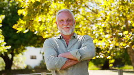 Portrait-Of-Smiling-Senior-Man-Standing-Outdoors-In-Garden-Park-Or-Countryside