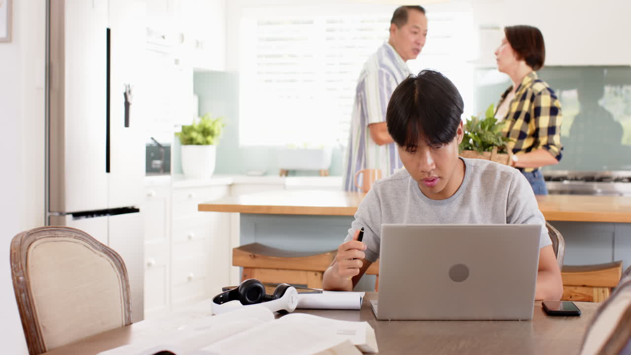 Working from home, young Asian man using laptop and writing in notebook