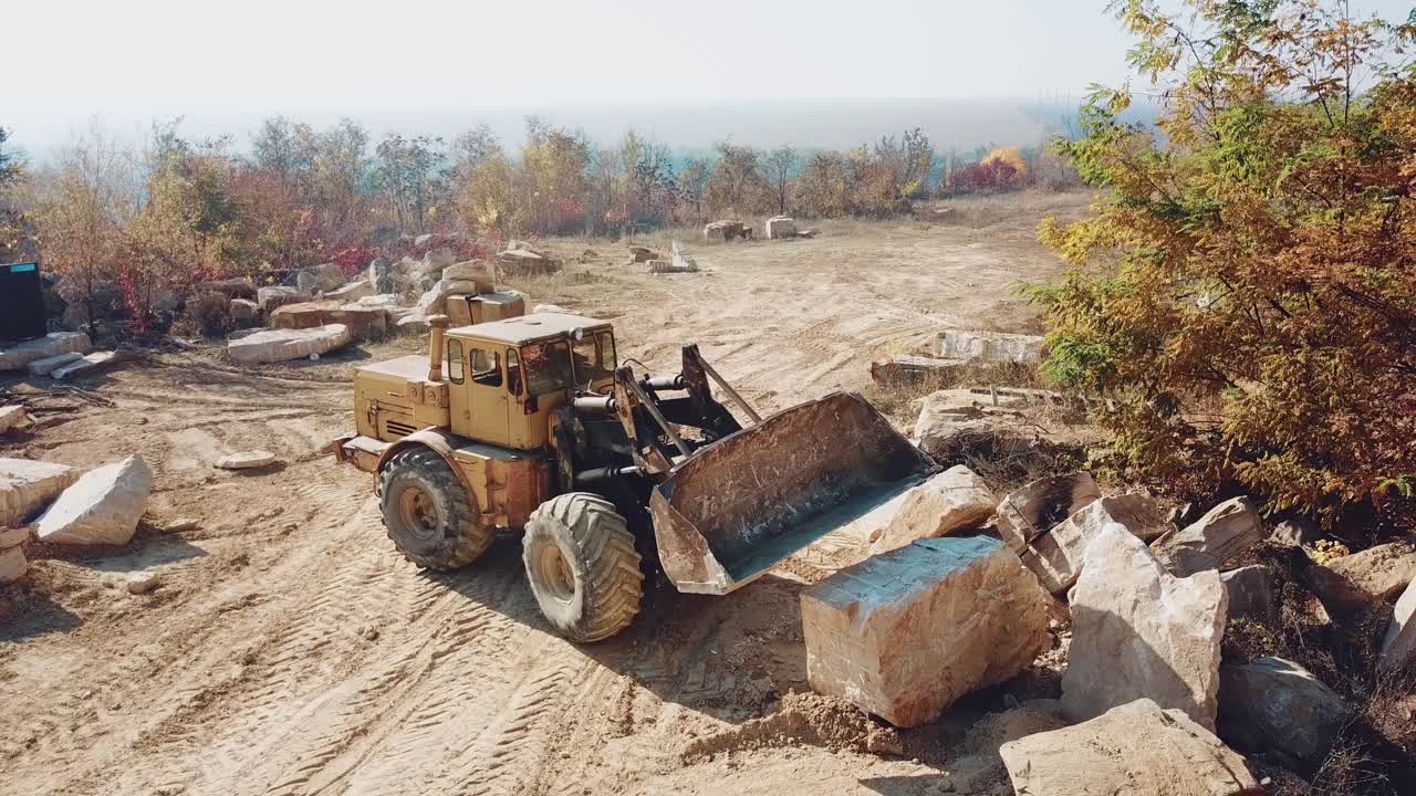 professional yellow bulldozer with a bucket is working in the quarry with stones on the background of sand. Close-up