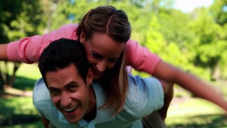 Handsome-man-giving-his-girlfriend-a-piggyback-ride-in-the-park