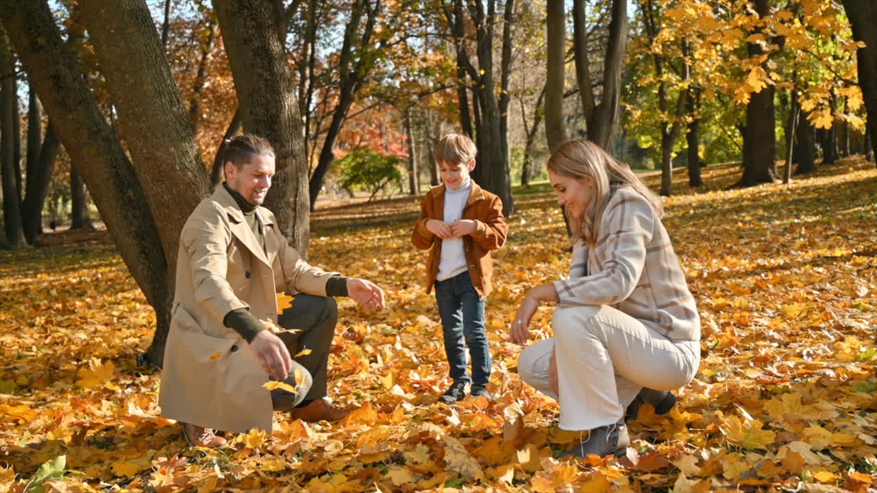 Happy family in an autumn park. Mother, father and son are throwing yellow leaves into the air. Slow motion