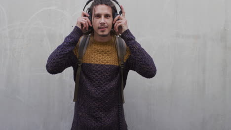 retrato relajado joven de raza mixta hombre se pone auriculares escuchando música sonriendo disfrutando de la satisfacción fondo de pared de hormigón