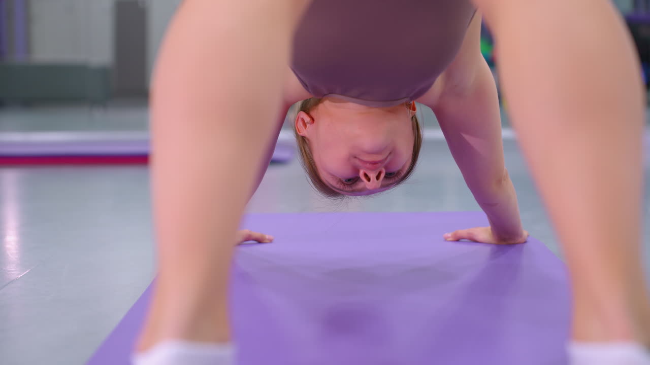 primer plano de una mujer haciendo ejercicio en una alfombra púrpura en un gimnasio moderno, equipos de gimnasio, reflejos en el espejo y iluminación brillante mejoran el entorno de entrenamiento