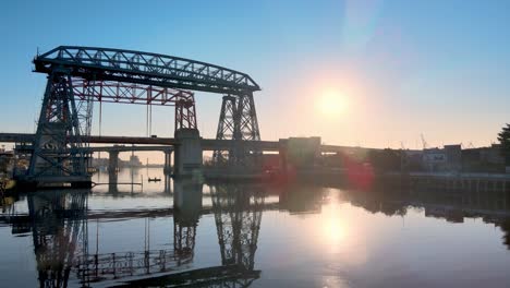 Low-Level-Luftaufnahme-Der-Fährbrücke-Nicolas-Avellaneda-über-Den-Matanza-Fluss-Bei-Sonnenaufgang-Mit-Sonneneruption