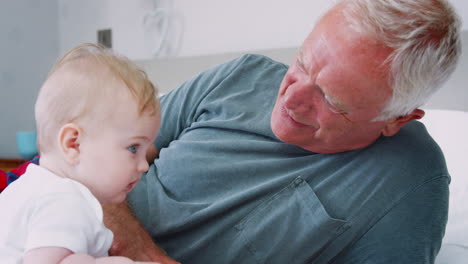 grandfather lying in bed at home looking after baby grandson