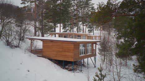 pequeña casa de madera con grandes ventanales construida sobre una pendiente nevada