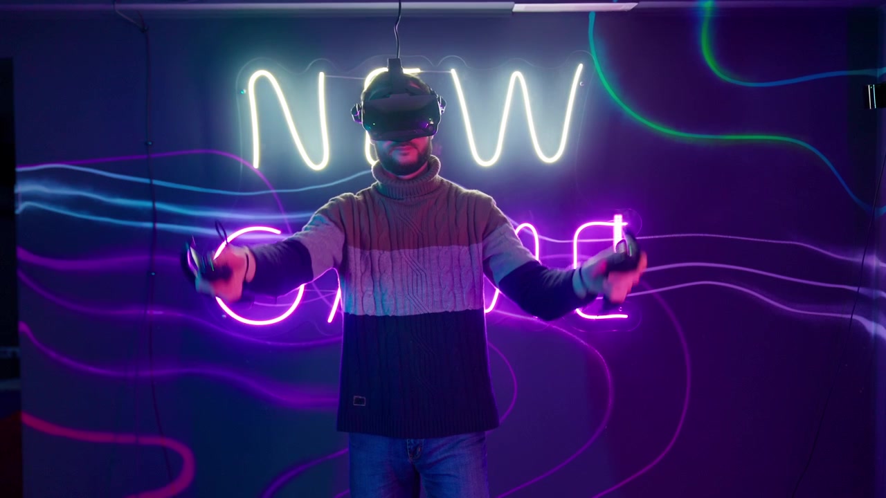 Mies pelaamassa virtuaalitodellisuuspeliä ohjaimilla neonvaloin valaistussa huoneessa