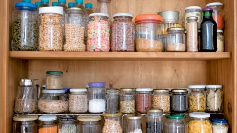 glass jars with different kinds of dry food stored on shelves in home kitchen, rising shot