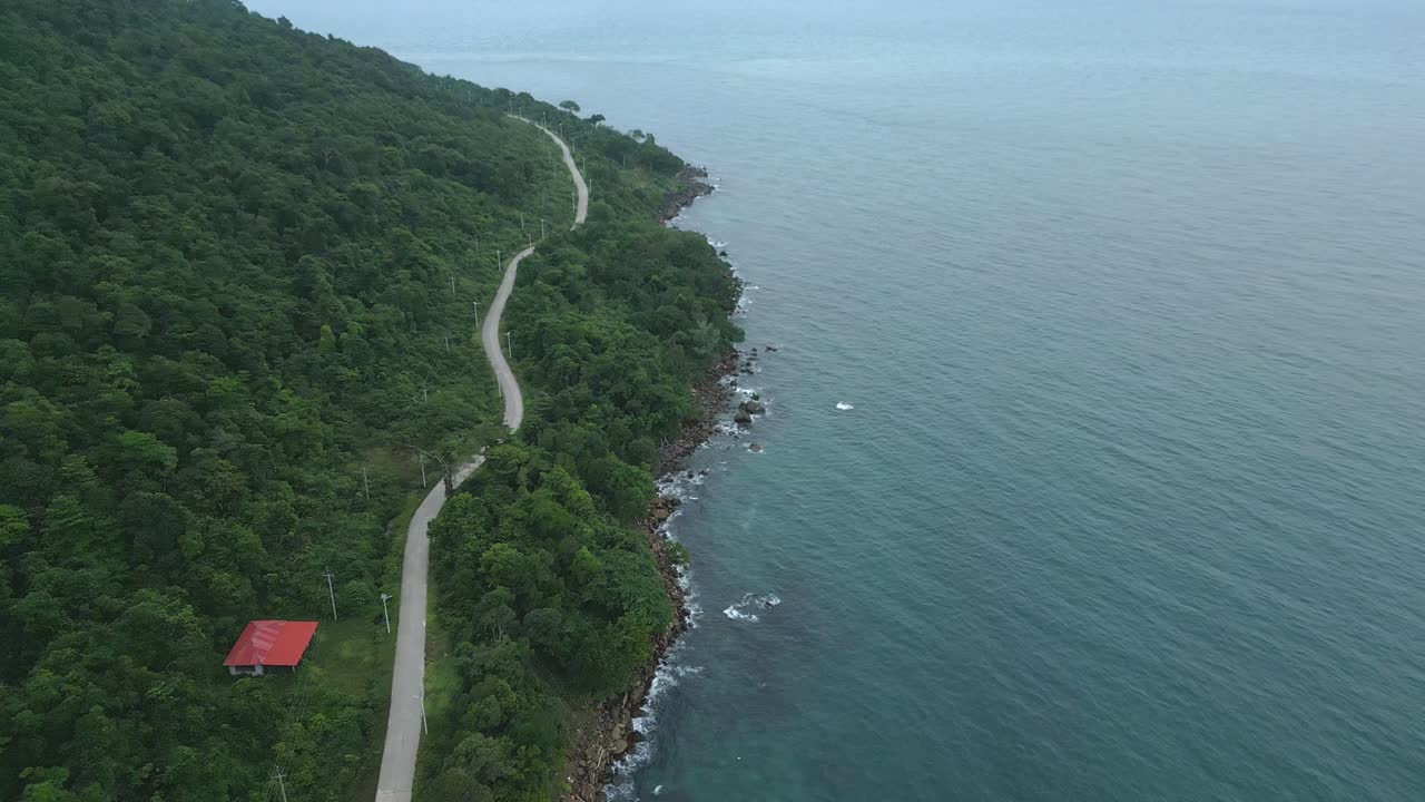 A small road winds along the coastline, camera pushing forward and descending towards the ocean.