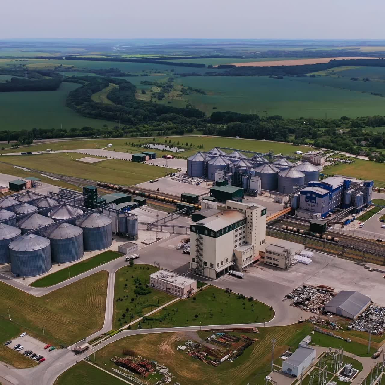Riesiger, moderner Getreidetrocknungskomplex im ländlichen Raum. Panoramablick auf das große Agrarunternehmen. Landwirtschaftliche Felder und Wälder im Hintergrund.