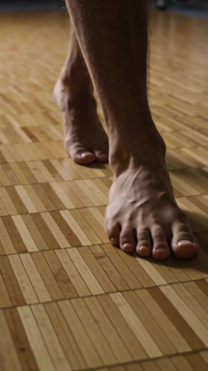 Video verticale: Piedi che si preparano a fare un passo avanti su pavimento in parquet, con ombre e banda sfocata.
