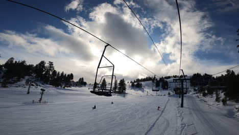 POV-Riding-on-Ski-Lift-in-Snowy-Terrain-and-Cloudy-Blue-Sky,-SLOW-MOTION