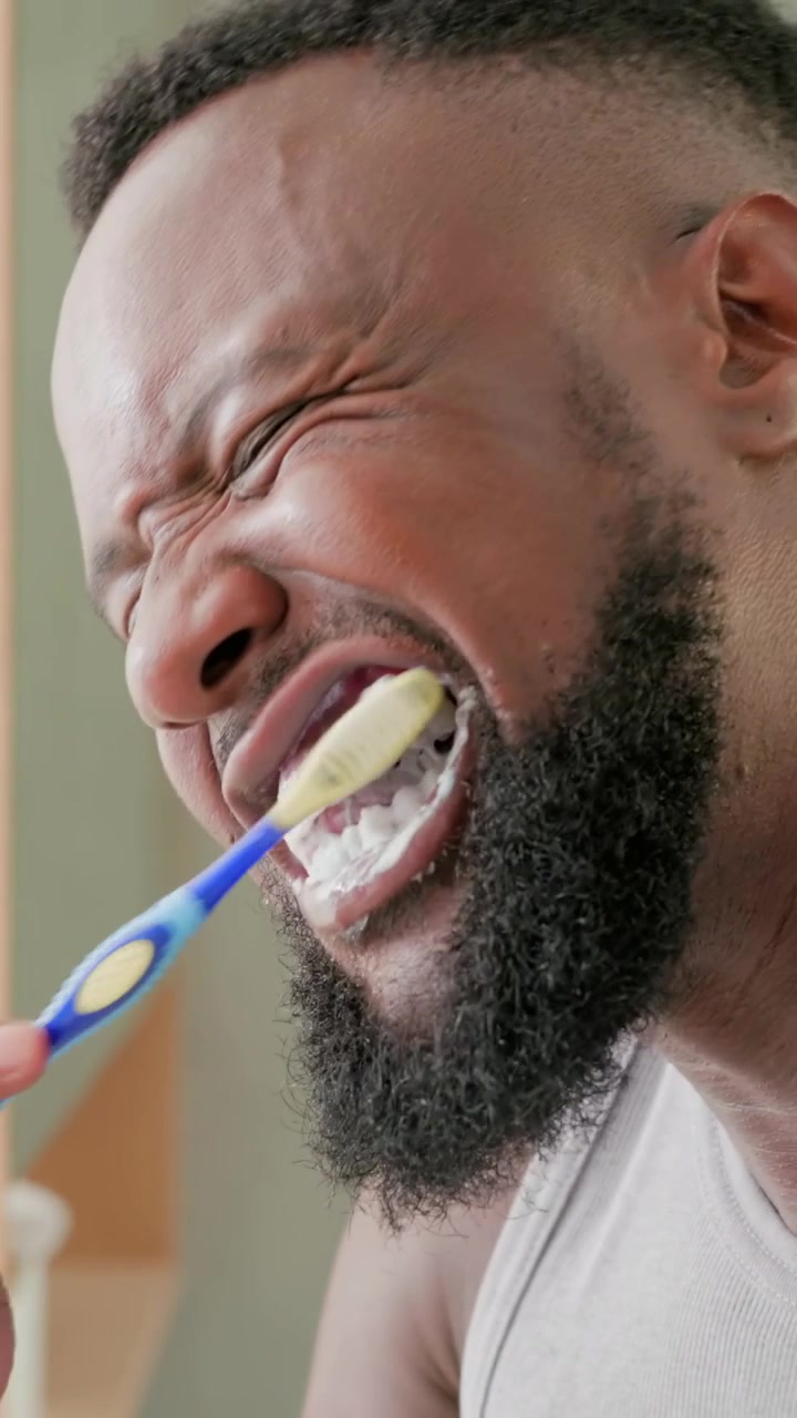 Vertical video: Brushing man in tank bringing blue brush, scrubbing teeth to clean at bathroom sink