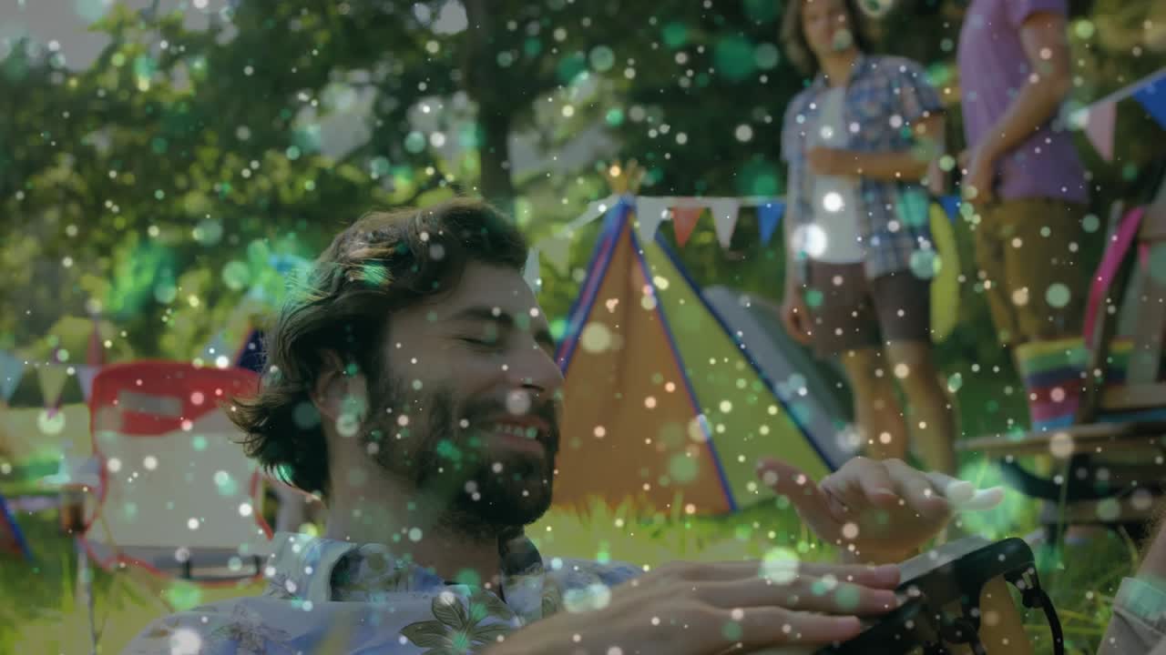 Bearded man playing music on hand drum for friends, while camera revealing tent, bokeh overlay