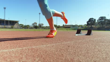 Caucasian-female-athlete-taking-starting-position-and-running-on-a-running-track-at-sports-venue-4k