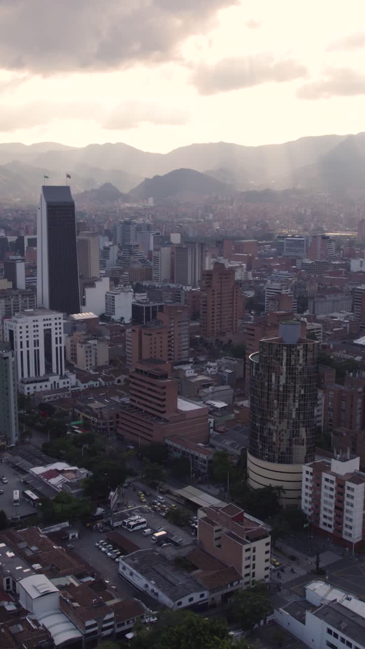Aerial view of Medellin cityscape at sunset, with modern buildings and mountains in the background. Vertical Video