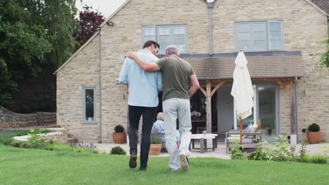 rear view of senior father with adult son walking in garden together