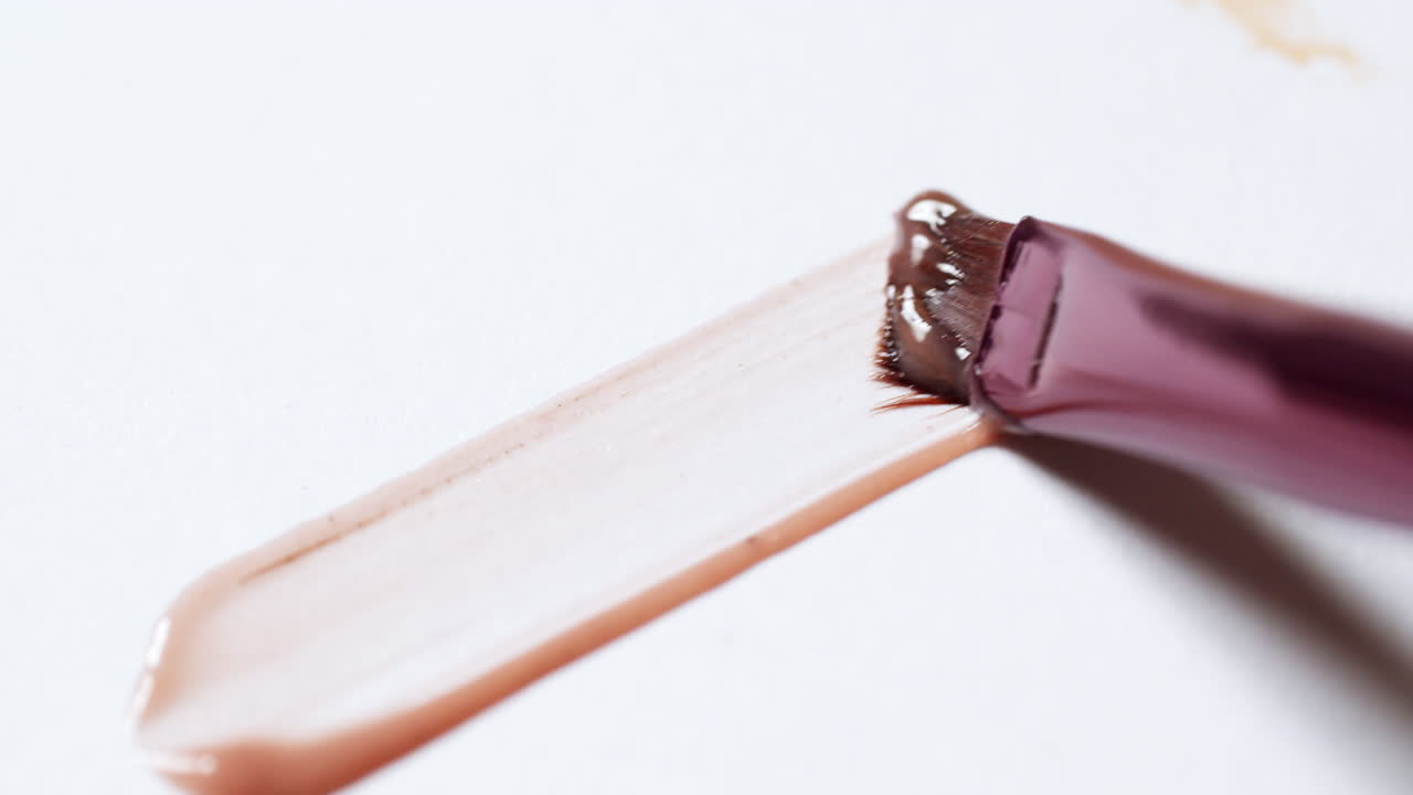 Applicazione di una linea di lucidalabbra lucido con un pennello applicatore su una tavolozza bianca semplice.