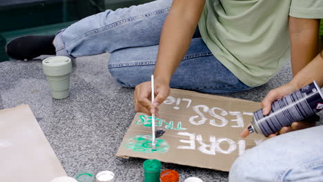 Woman-Painting-Board-With-Brush-And-Her-Friend-Is-Spraying