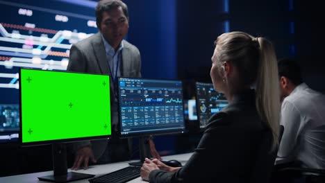 especialista femenina trabaja en una pantalla verde, conversa con el gerente de proyecto en una gran sala de control de infraestructura. el equipo de la sala de monitoreo de profesionales utiliza computadoras que muestran gráficos, información