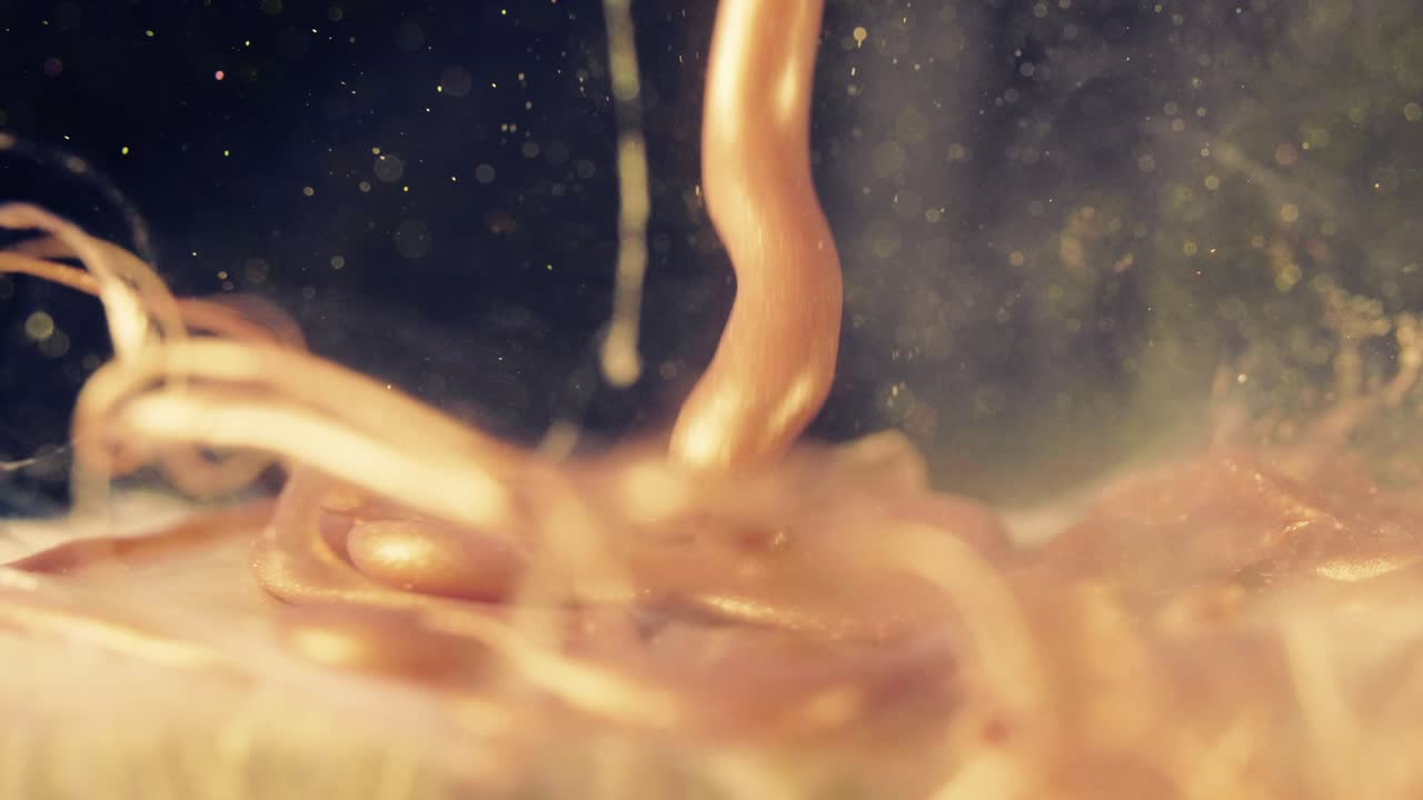 황금 잉크 입자는 검은 바탕에 다채로운 혼란으로 물에 흐른다.