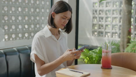 woman using phone and taking notes in cafe