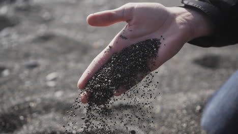 black sand of perissa, greece slowly falling out of mans hands, slow motion