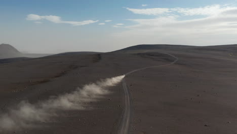 Top-view-of-majestic-Iceland-landscape-with-car-driving-rock-highlands.-High-angle-view-car-driving-fast-motorway-stirring-up-dust-cloud.-Insurance-commercial