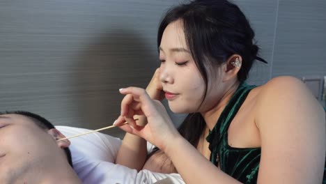 woman gently cleaning man's ear in bed