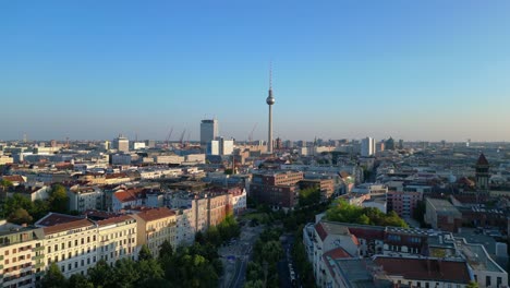 berlin tv tower rising above rooftops and a construction site at senefelderplatz during sunset. amazing aerial view flight fly push forward drone