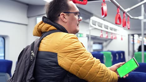 back view of man watch smart phone with green screen and browsing online in train. mock up for watching content on cell phone. blank digital phone in hand of guy standing indoors in public transport