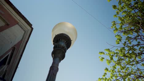 old city street tilt up to street lamp bulb with blue sky and green leaves