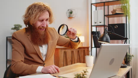 business man working at home office holding magnifying glass looking at laptop screen wow expression