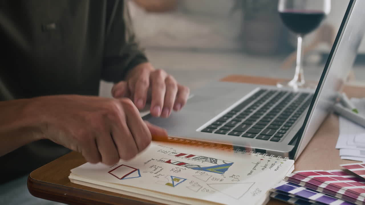 Anonymous Designer Sketching in Copybook at Table with Laptop