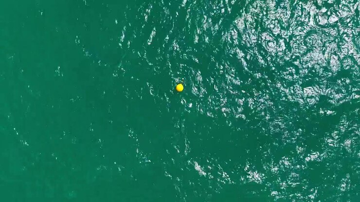 Floating yellow buoy in deep green water under bright sunlight