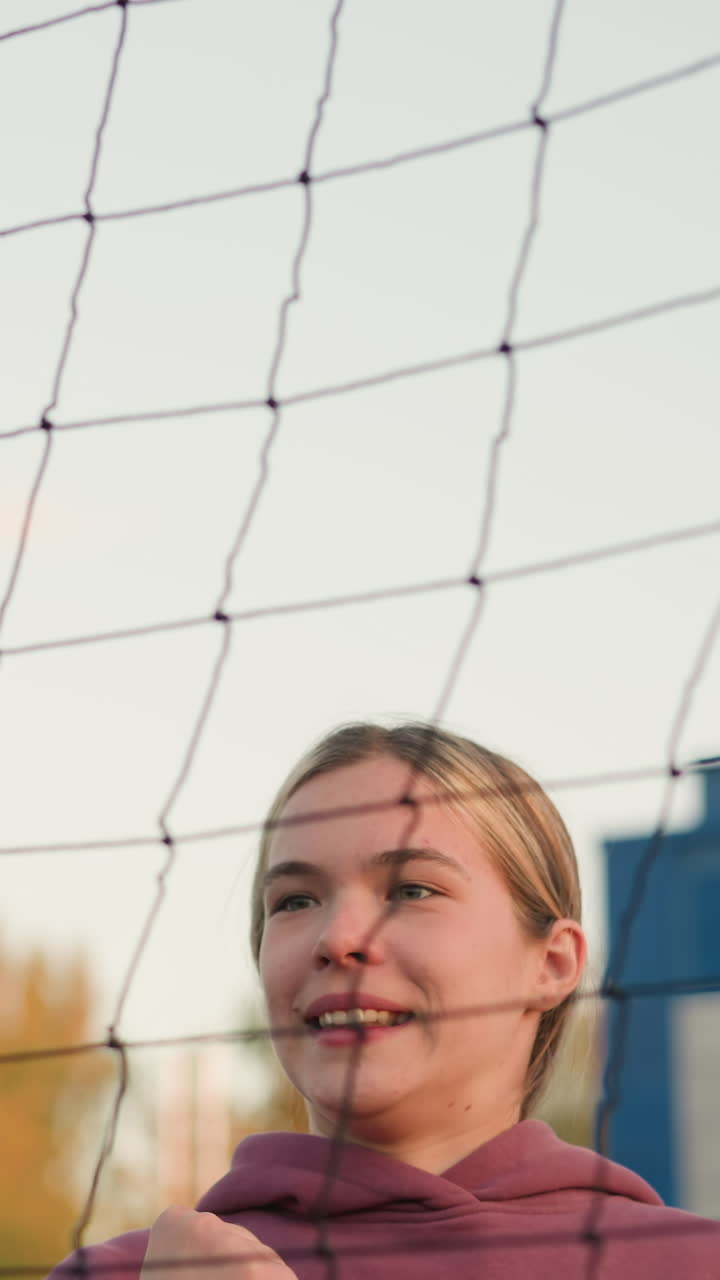 젊은 여성 운동선수가 점프하는 클로즈업, 집중과 결단력으로 배구 타격 준비, 승리를 보여주는, 배경에 배구 망과 멀리서 볼 수 있는 건물